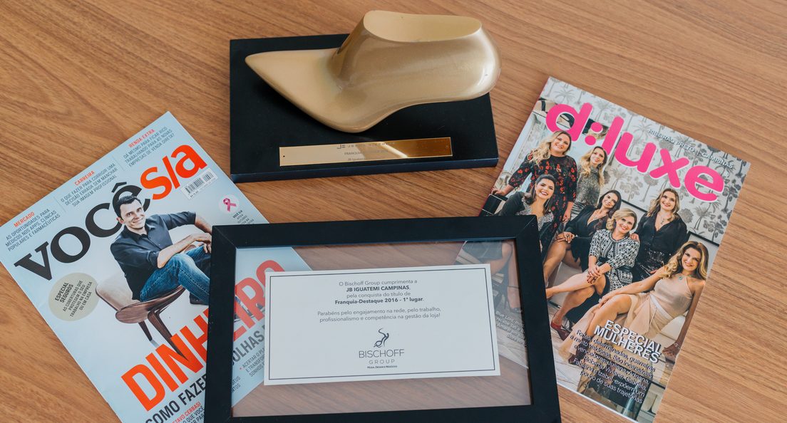 O troféu dourado, o certificado de Franquia-Destaque 2016 e revistas sobre uma mesa de madeira.